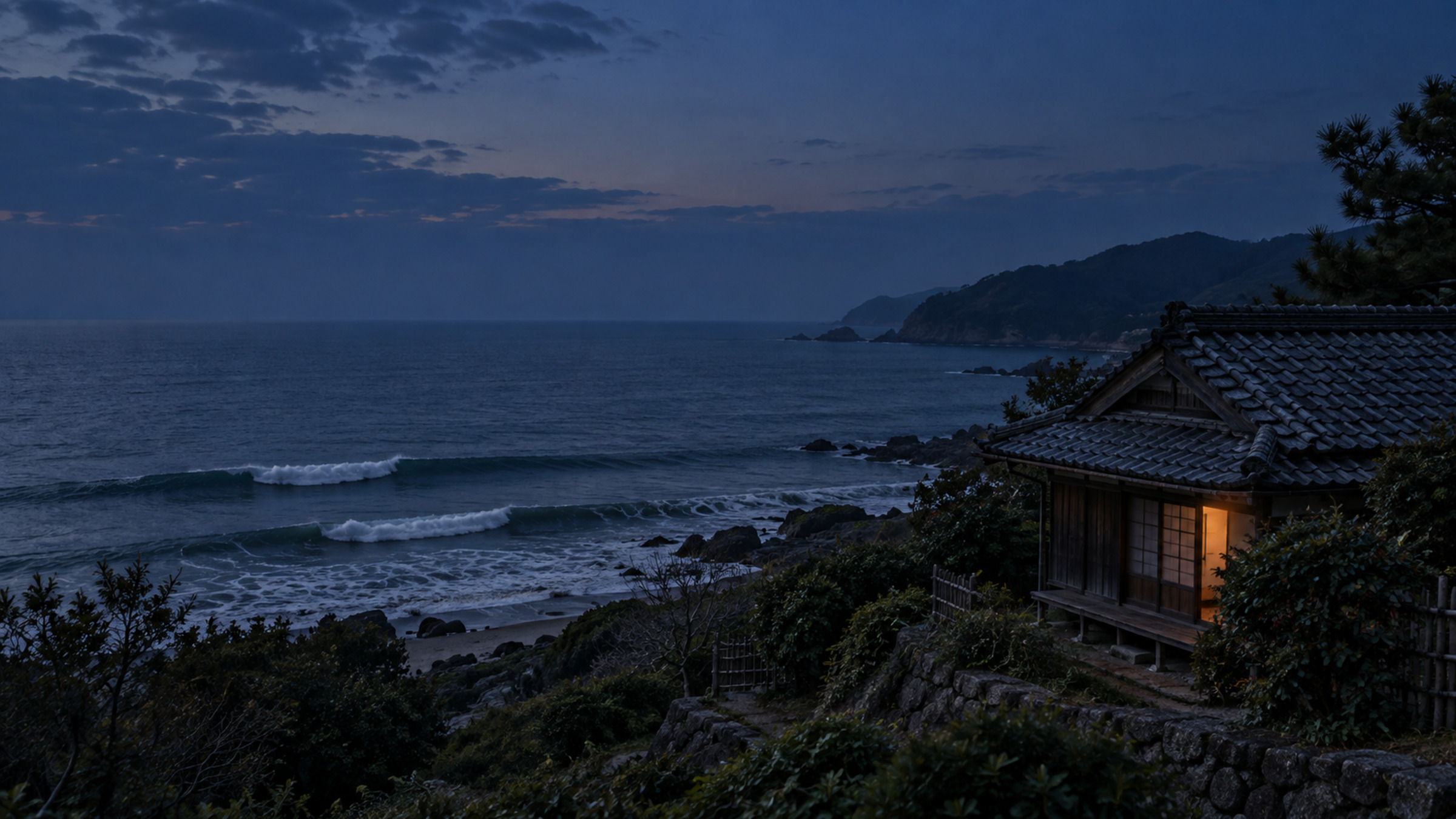 傍晚的海岸，坡上一棟日式木屋亮著一格燈，海上兩道浪先後推上來